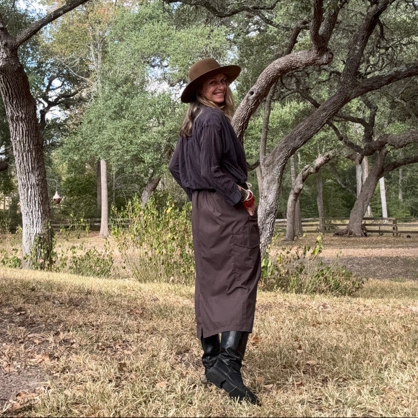 Person in a long coat and hat standing among trees in a natural setting