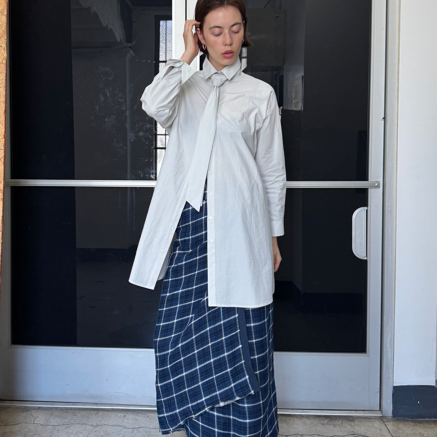 Woman in a white shirt and blue plaid skirt standing in front of a door with number 206.