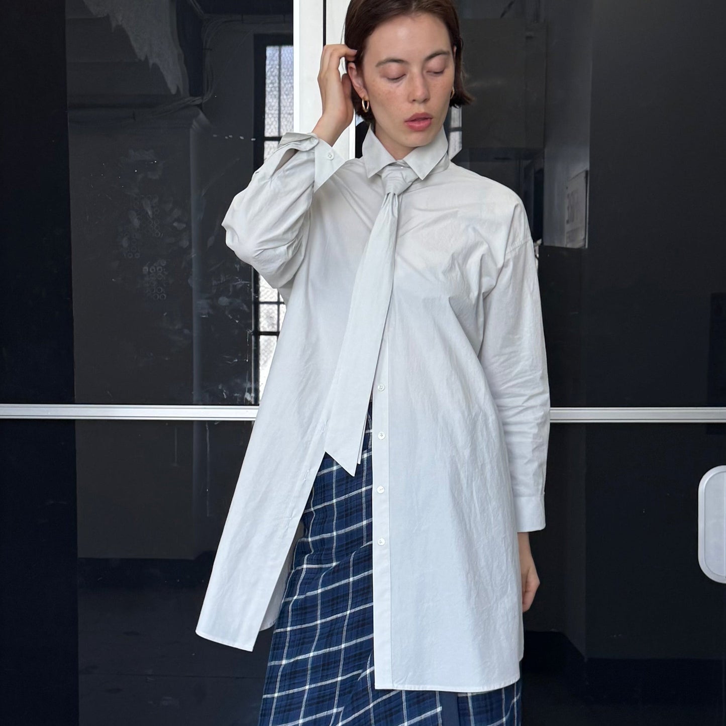 Woman in a white shirt and blue plaid skirt standing in front of a door with number 206.