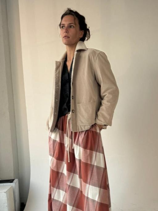 Person wearing a beige jacket and red plaid pants against a plain wall.