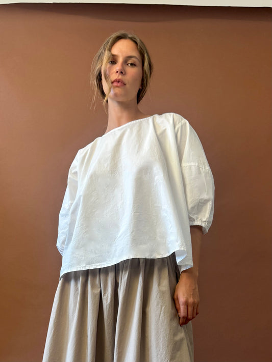 Person wearing a white blouse and beige skirt against a brown background