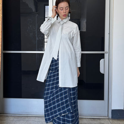 Woman in a white shirt and blue plaid skirt standing in front of a door with number 206.